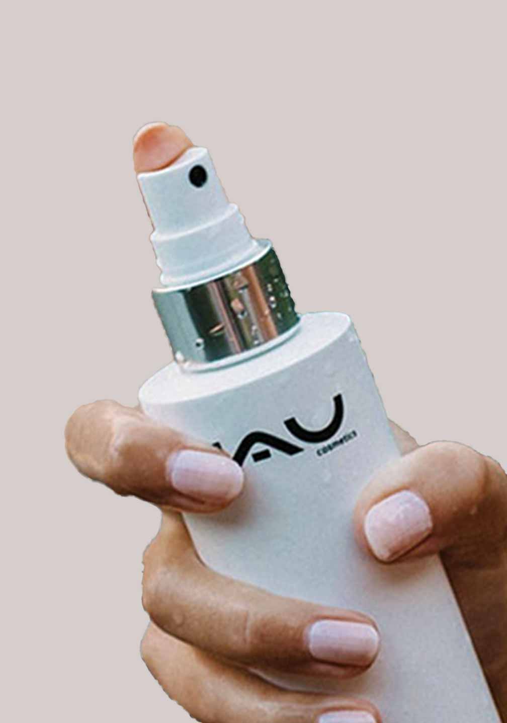 Hand hält eine moderne silberfarbene Sprühflasche mit der Aufschrift „VAU“ und einer Düse zur Hautpflege.